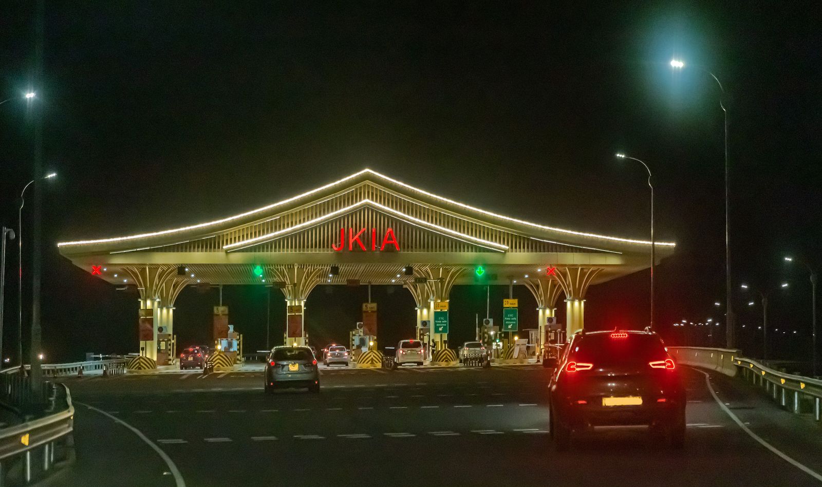Cars passing the illuminated JKIA toll plaza on the Nairobi Expressway at night