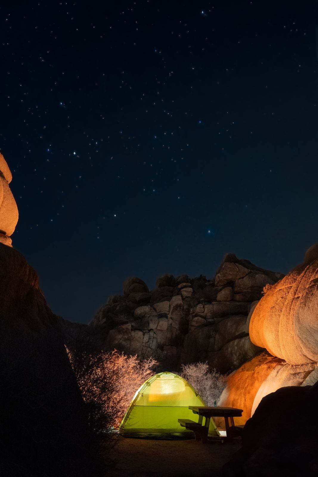 A lit tent pitched among rocks beneath a star-filled night sky